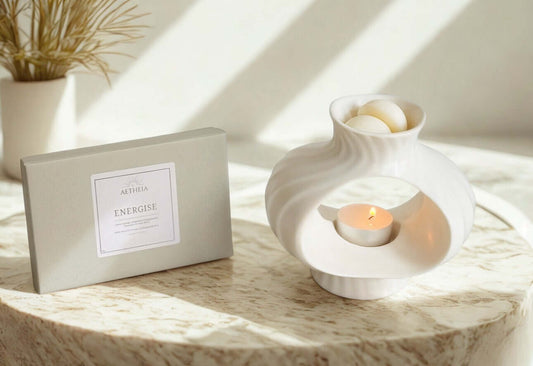 White ceramic wax melt burner with lit candle and Aetheia’s energise wax melt box on a marble top surface