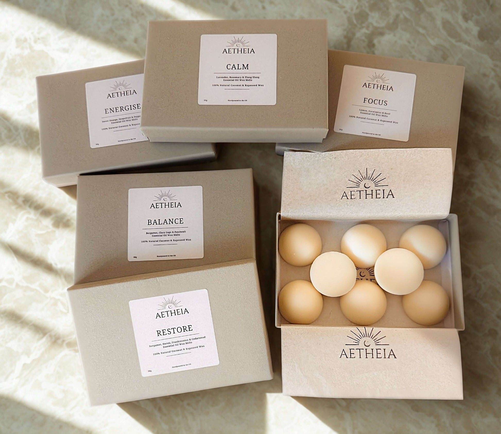 Aetheia wax melt product packaging with various boxes and an open box containing round wax melts on a textured surface.